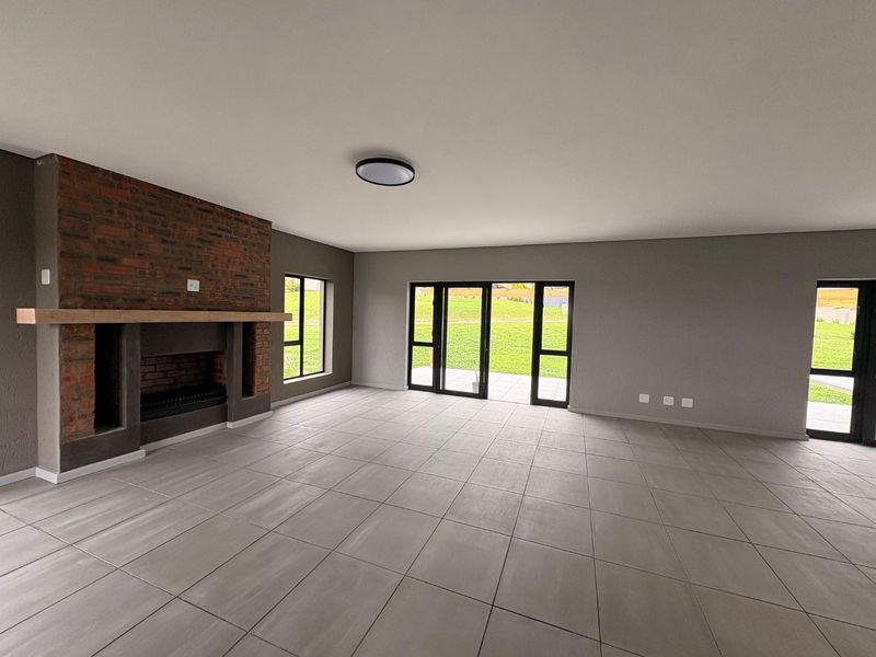 Spacious, modern living area featuring a prominent brick fireplace with timber mantel, large format floor tiles, and expansive glass doors opening to the garden.