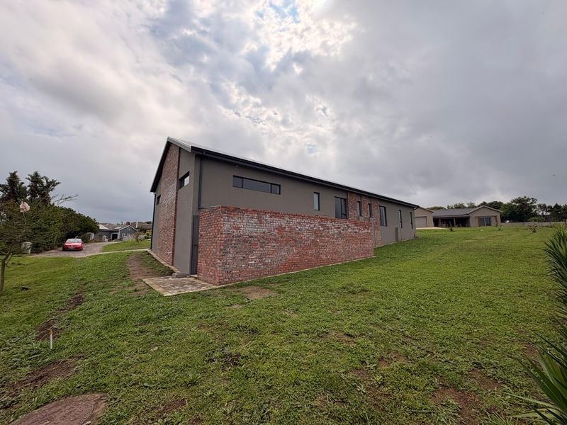 A modern residential exterior featuring a combination of dark grey rendered walls and exposed brickwork, set within a spacious grassed yard.