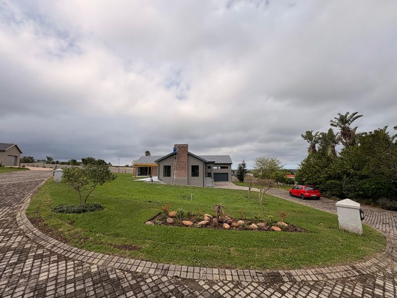 A modern single-story house featuring a prominent brick chimney, paved driveway, and well-maintained garden area.