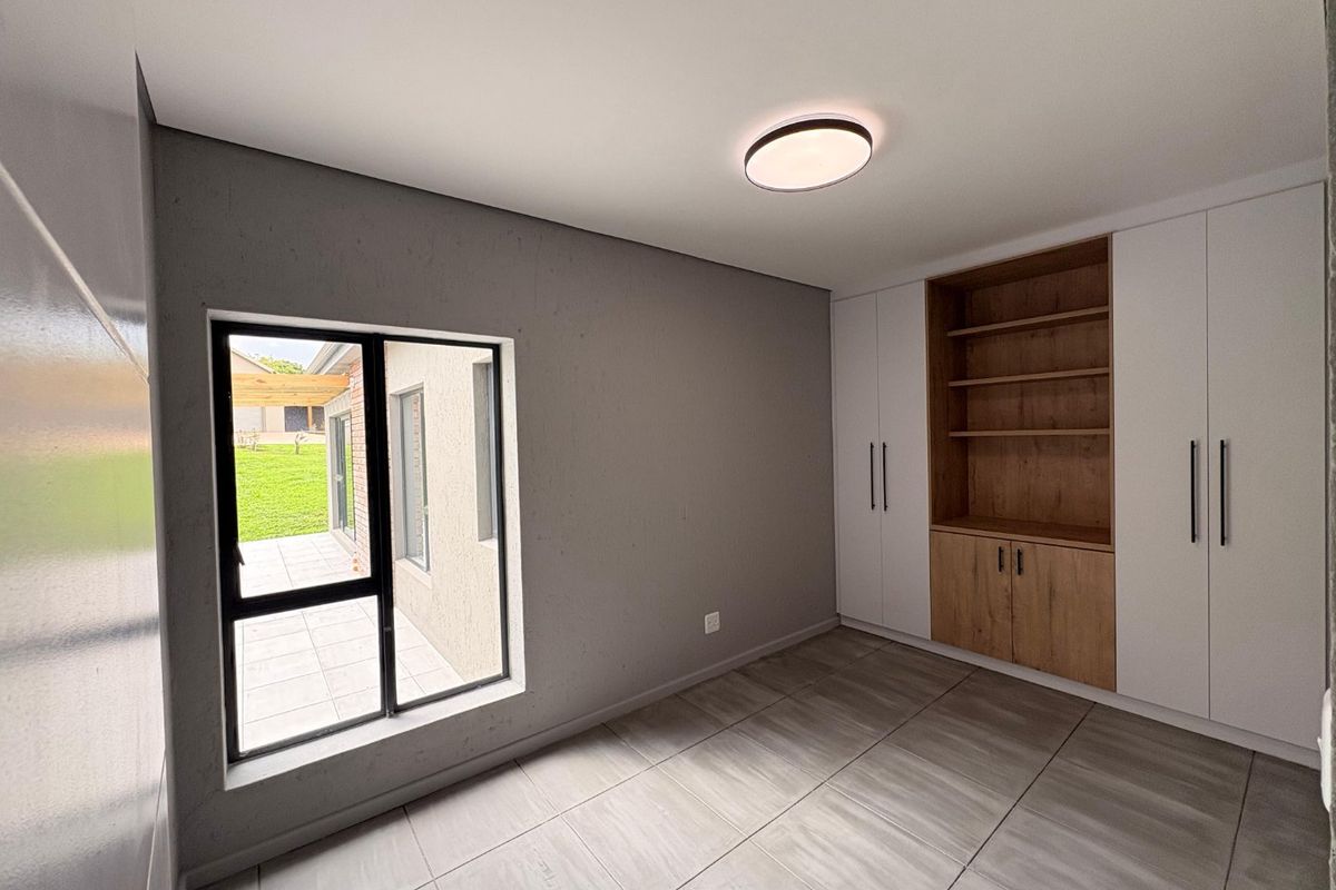 A modern, empty bedroom featuring neutral grey walls, tiled flooring, and extensive built-in cabinetry with integrated shelving and storage.