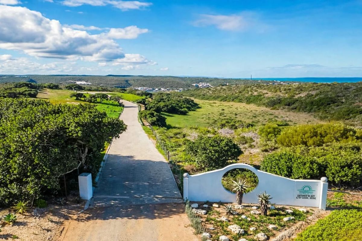 Aerial view of the estate entrance featuring a paved driveway, landscaped surroundings, and coastal landscape in the distance.