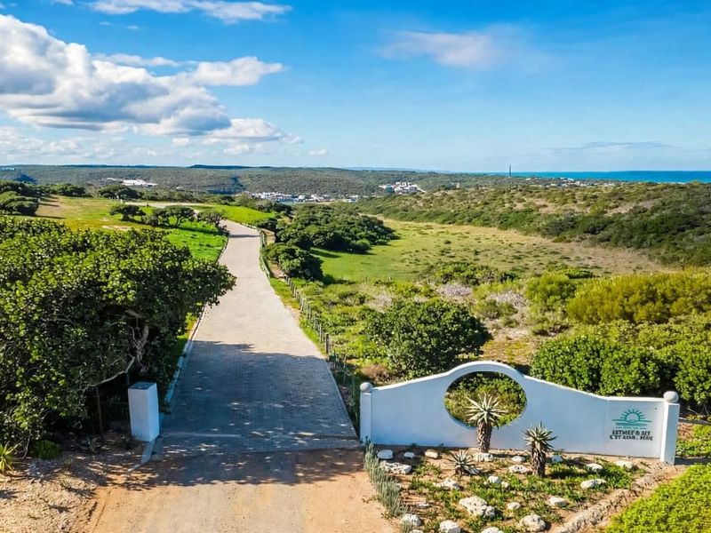 Aerial view of the estate entrance featuring a paved driveway, landscaped surroundings, and coastal landscape in the distance.