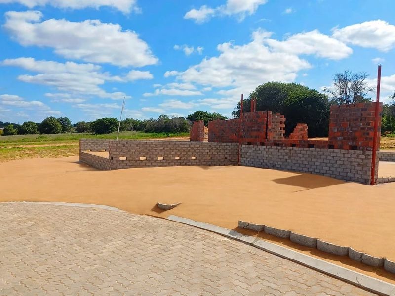 A property under construction showing a paved driveway and the initial brickwork of the building structure on a large plot of land.