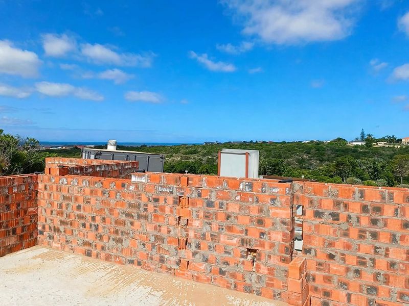 An elevated view of an unfinished construction site featuring exposed brick walls and a concrete slab, overlooking a coastal landscape.