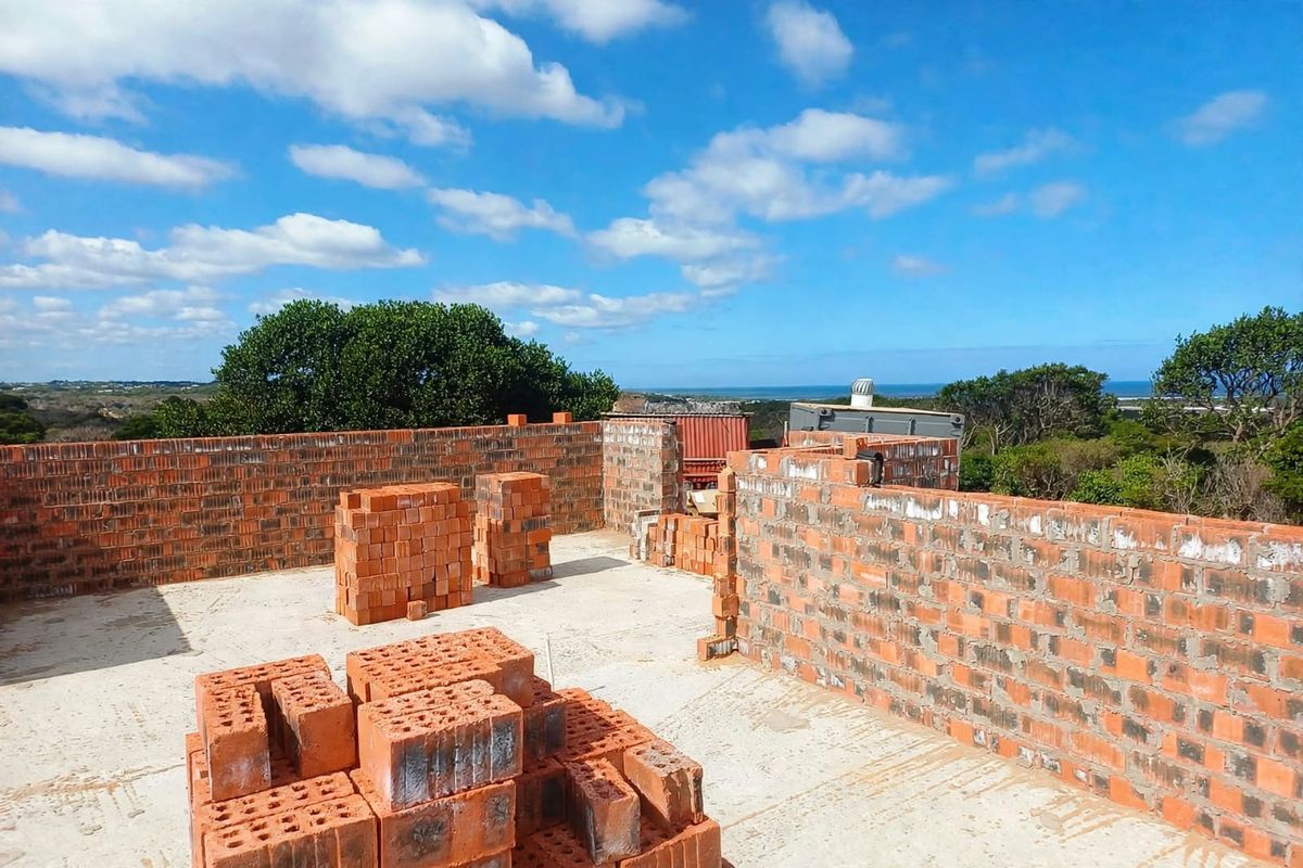 An elevated view of a property under construction, featuring exposed brick walls and a concrete slab foundation with coastal views.