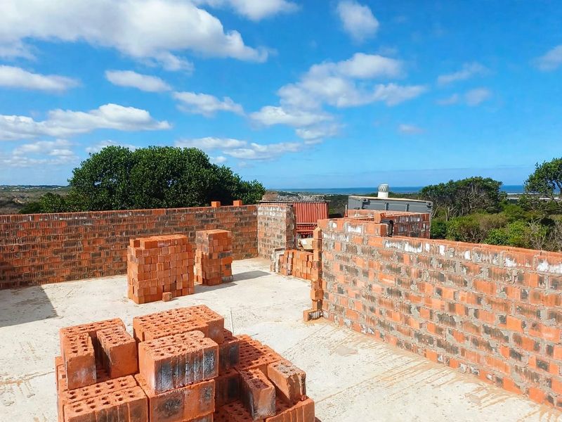 An elevated view of a property under construction, featuring exposed brick walls and a concrete slab foundation with coastal views.