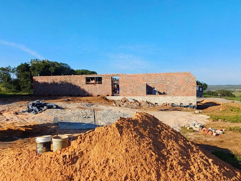 A view of a residential property currently under construction, featuring exposed brick walls and open window and door frames on a large plot.
