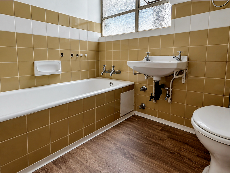 A functional bathroom featuring a bathtub, wall-mounted basin, and toilet, finished with retro-style ceramic wall tiles and wood-look laminate flooring.