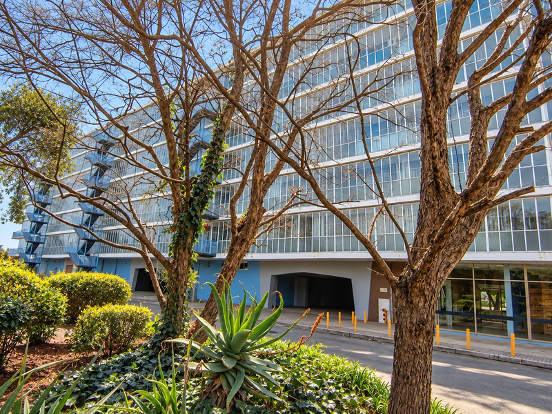 Exterior view of a multi-story apartment building featuring a large glass facade, external staircases, and ground-level covered parking area.