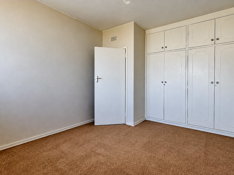 A bright, empty bedroom featuring neutral walls, carpeted flooring, and extensive built-in cupboard storage.