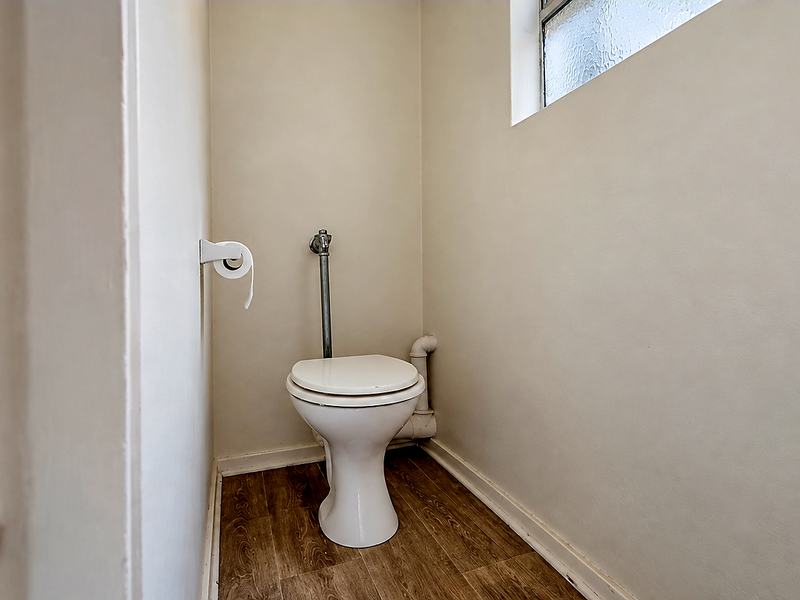 A compact, functional guest toilet featuring laminate flooring, a standard white toilet suite, and an obscured glass window for privacy.