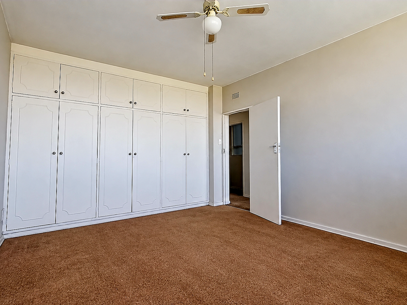 A spacious, empty bedroom featuring extensive built-in cupboards, a ceiling fan, and carpeted flooring.