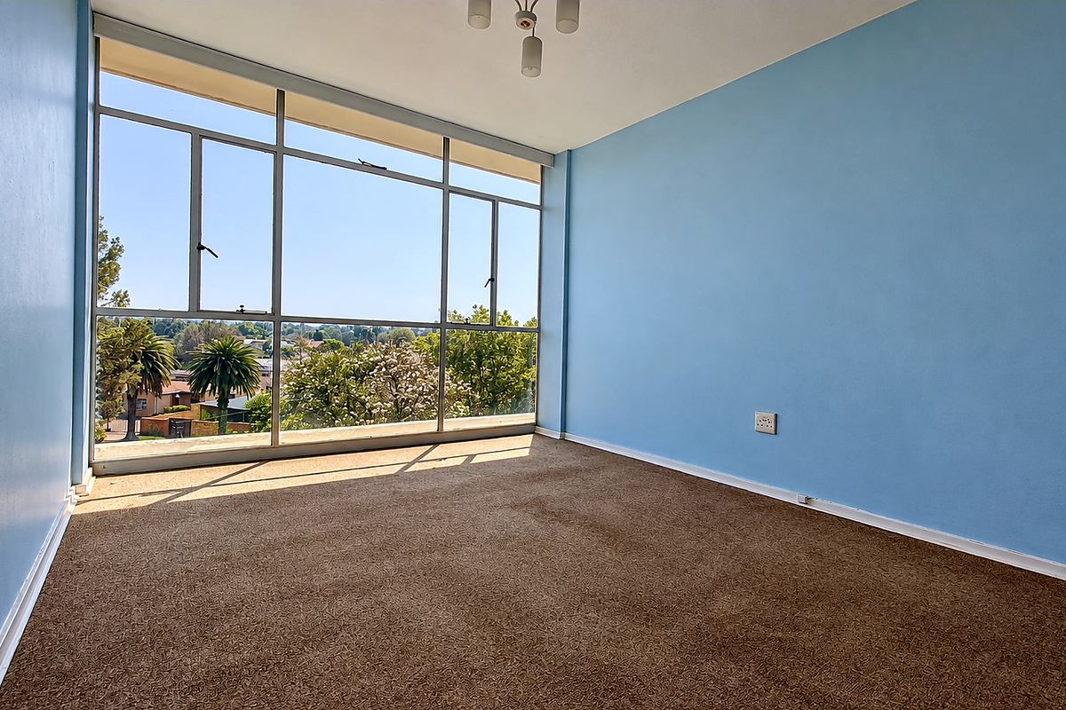A bright, empty bedroom featuring large floor-to-ceiling windows that provide ample natural light and pleasant neighborhood views.