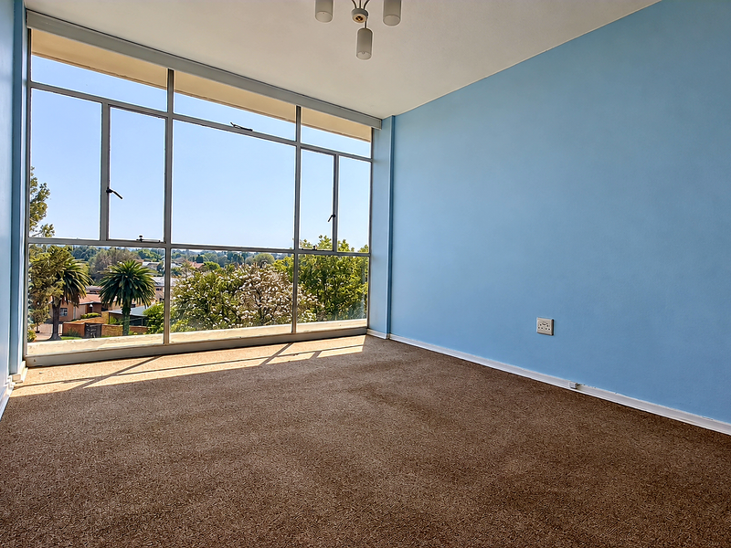 A bright, empty bedroom featuring large floor-to-ceiling windows that provide ample natural light and pleasant neighborhood views.