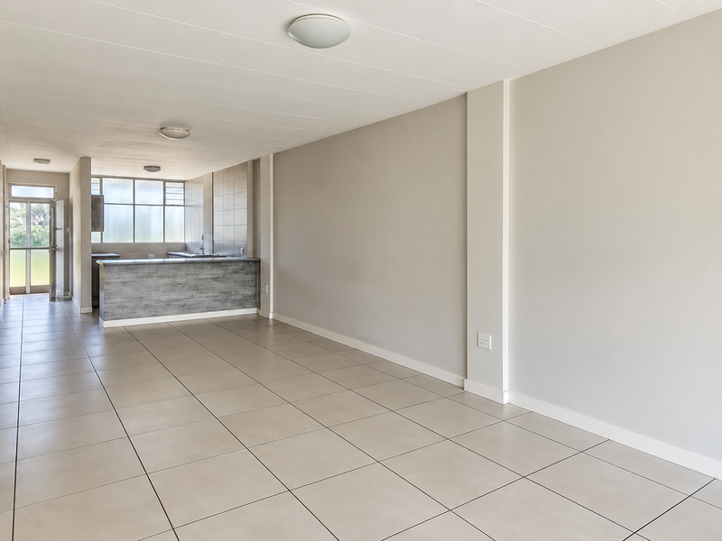 An open-plan living and kitchen area featuring neutral tiled flooring, a breakfast bar, and a functional kitchen layout with ample natural light.