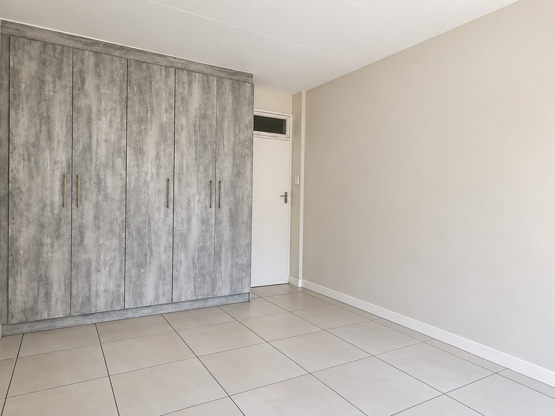 A bright, empty bedroom featuring modern grey wood-look built-in cupboards and neutral tiled flooring.
