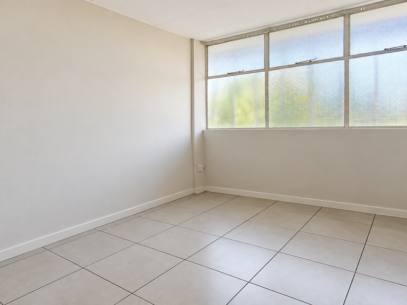 A bright, empty bedroom featuring neutral tiled flooring and a large multi-pane window providing ample natural light.