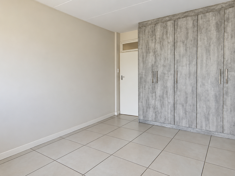 A clean, empty bedroom featuring neutral tiled flooring and modern grey wood-look built-in cupboards.