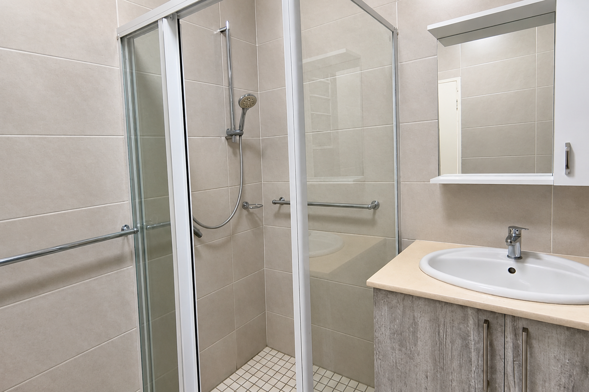 A clean, modern bathroom featuring a glass shower enclosure, vanity with integrated washbasin, and wall-mounted mirror cabinet with neutral wall tiling.