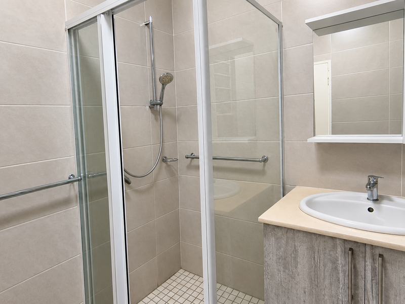 A clean, modern bathroom featuring a glass shower enclosure, vanity with integrated washbasin, and wall-mounted mirror cabinet with neutral wall tiling.