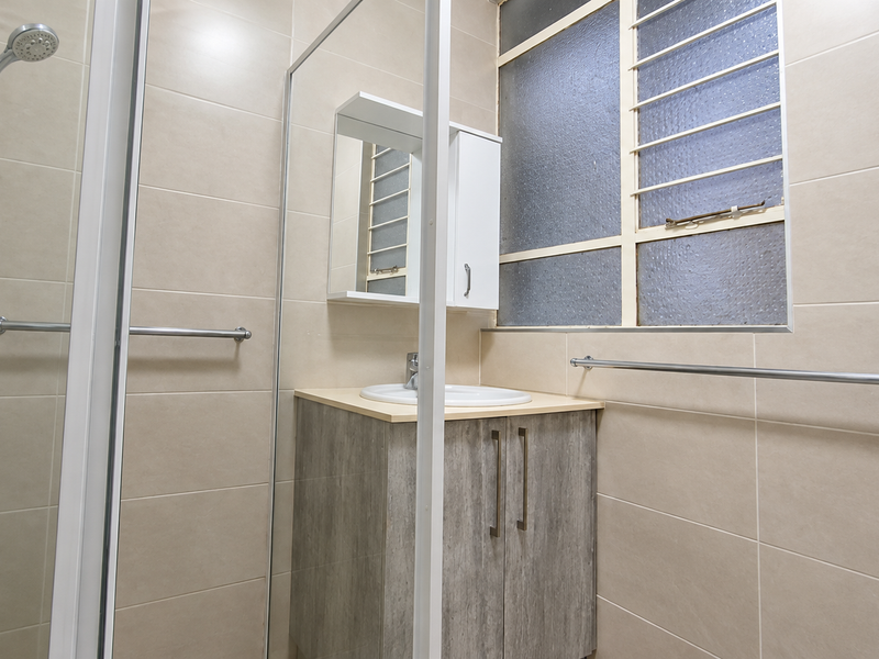 A functional bathroom featuring a shower enclosure, vanity cabinet with basin, and tiled walls, providing a clean and practical space.