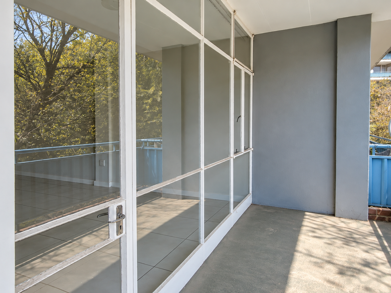 A spacious covered balcony featuring large glass sliding doors, tiled flooring, and a blue metal balustrade, offering a bright outdoor living space.