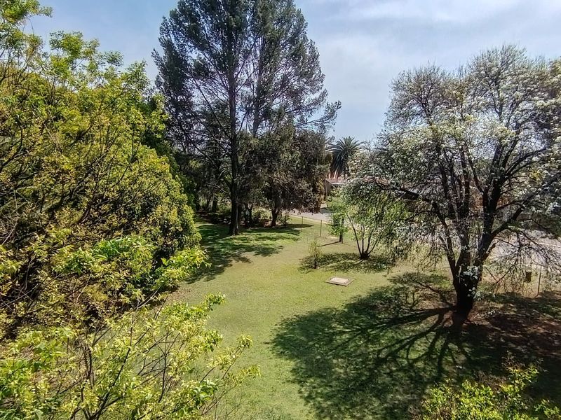 A scenic elevated view overlooking a lush green garden area with mature trees and well-maintained lawn.