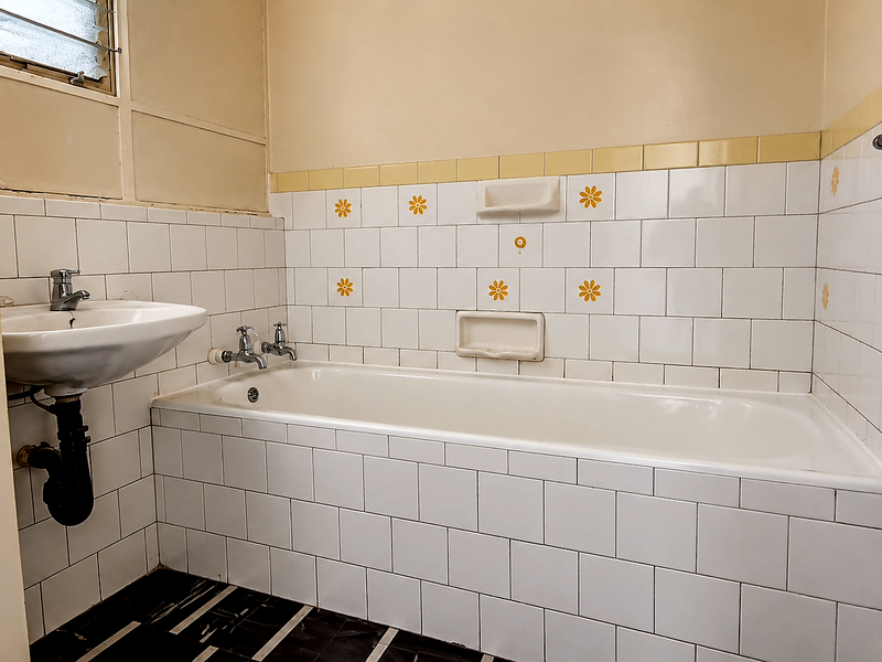 A dated bathroom featuring a built-in bathtub, wall-mounted basin, and original decorative wall tiles, offering potential for a modern renovation.