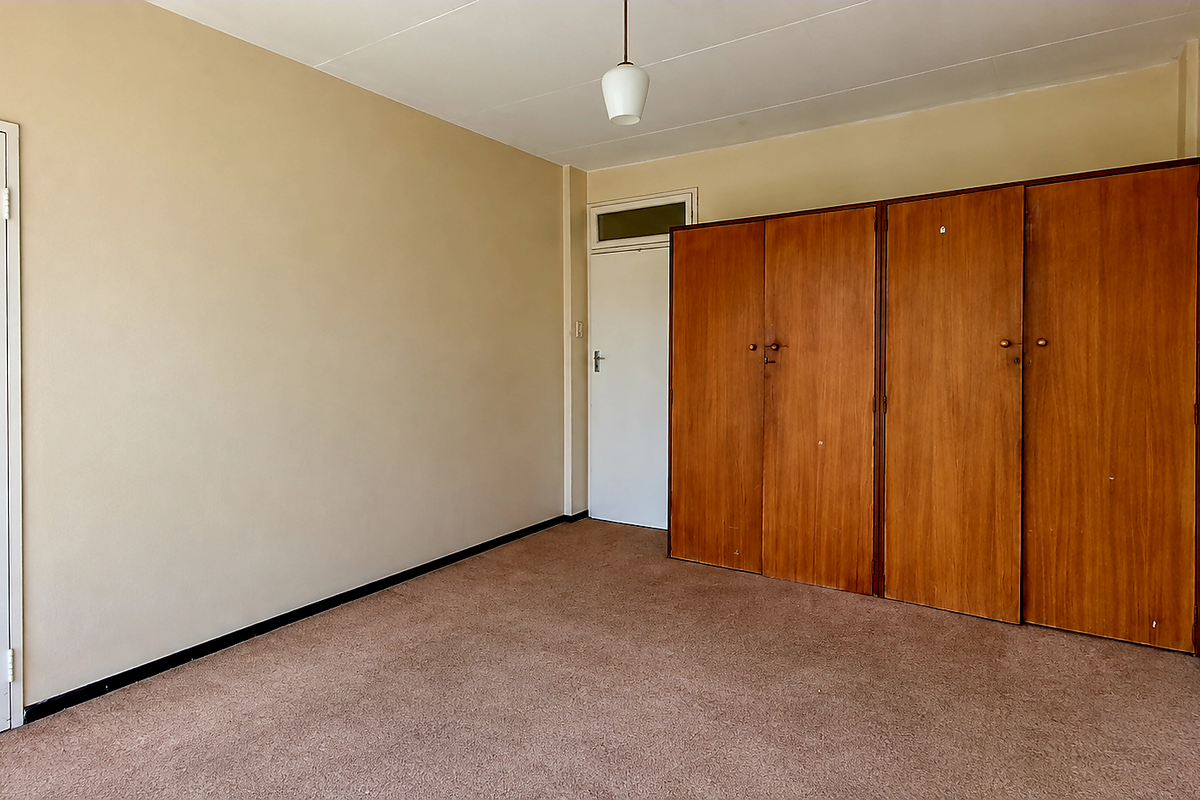 An empty bedroom featuring built-in wooden wardrobes, neutral wall paint, and carpet flooring, offering a blank canvas for renovation.
