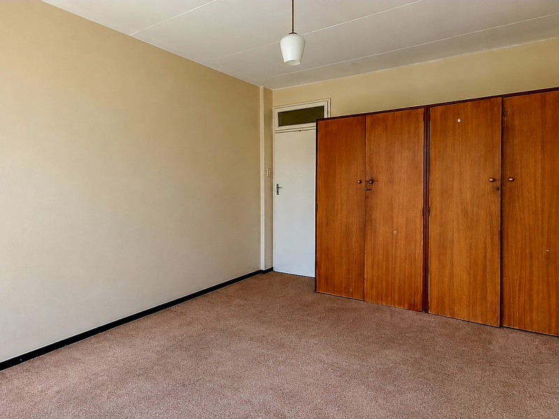 An empty bedroom featuring built-in wooden wardrobes, neutral wall paint, and carpet flooring, offering a blank canvas for renovation.