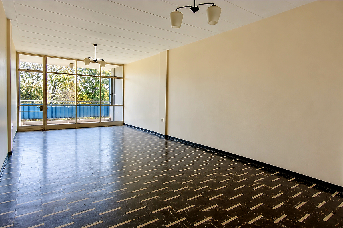 A spacious, empty living area featuring large glass sliding doors that provide natural light and access to an outdoor balcony.