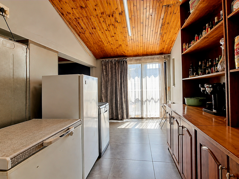 A functional scullery or utility area featuring timber-clad vaulted ceilings, tiled flooring, and extensive built-in wooden cabinetry with direct access to the outdoor area.