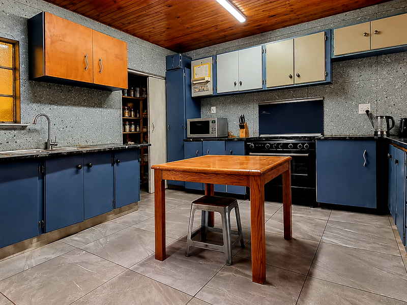 A functional kitchen featuring blue and wood-tone cabinetry, tiled walls, a built-in oven, and a dedicated pantry area with tiled flooring throughout.