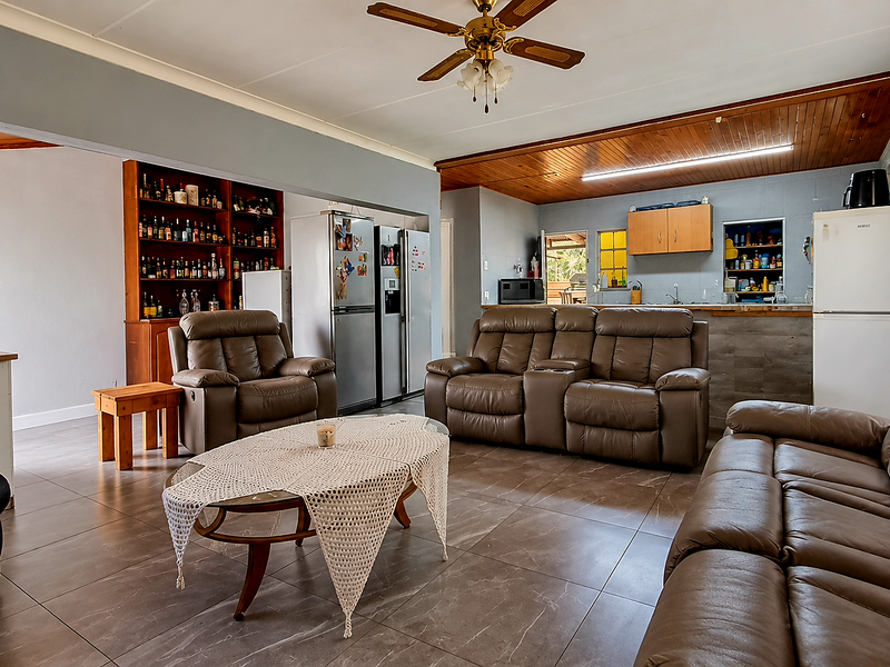 Spacious open-plan living and kitchen area featuring tiled flooring, timber ceiling accents, and a functional breakfast bar layout.