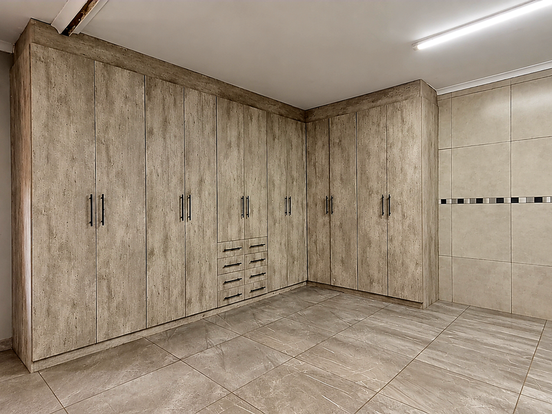 A spacious bedroom featuring extensive built-in wooden cabinetry, large format floor tiles, and a decorative tiled wall section.