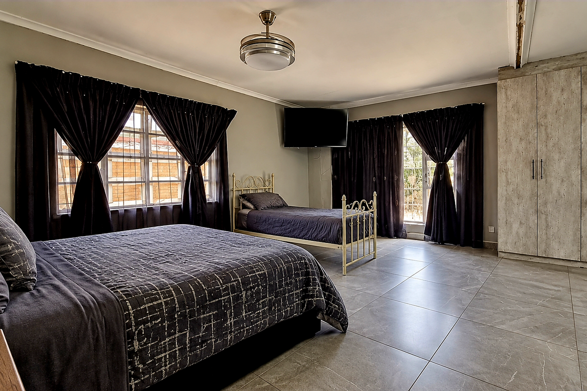 Spacious bedroom featuring large format floor tiles, built-in cupboards, and a ceiling fan, with security bars on the windows.