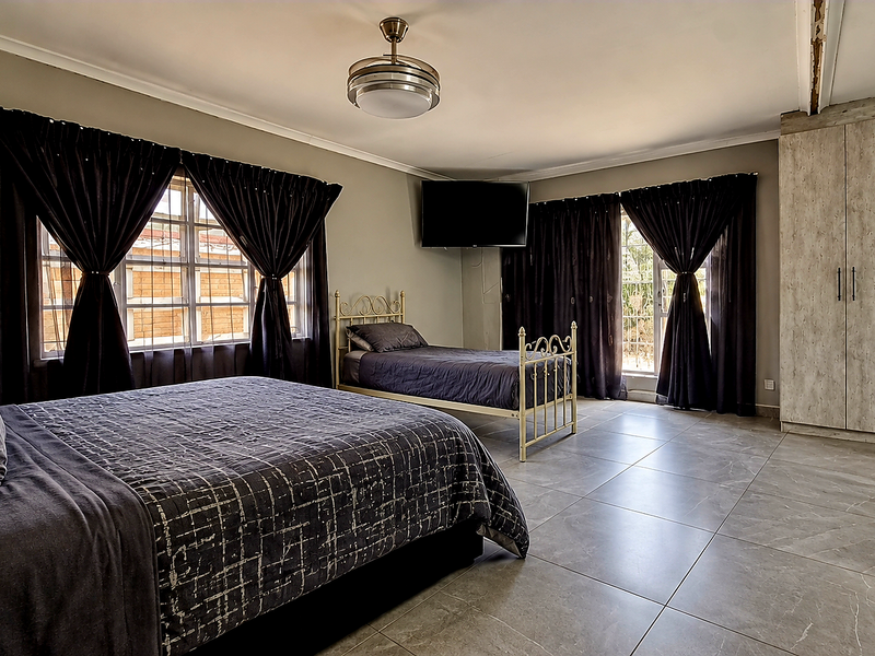 Spacious bedroom featuring large format floor tiles, built-in cupboards, and a ceiling fan, with security bars on the windows.