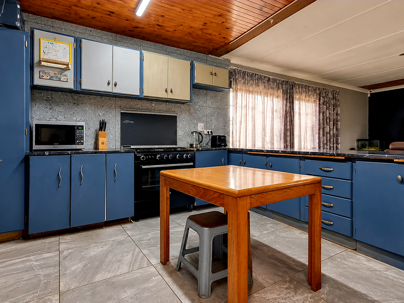 A functional kitchen featuring blue cabinetry, laminate countertops, a gas stove, and a timber-paneled ceiling, offering a dated but well-maintained workspace.