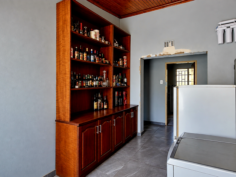 A functional scullery area featuring built-in wooden cabinetry, tiled flooring, a water filtration system, and a timber ceiling, with some minor wall finishing required.