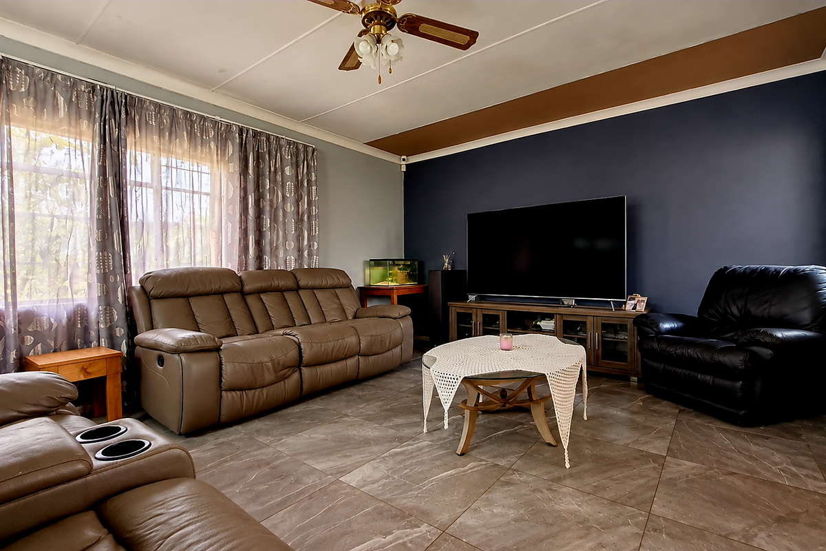 A spacious living room featuring tiled flooring, a ceiling fan, and a dark accent wall, providing a comfortable and functional family living space.