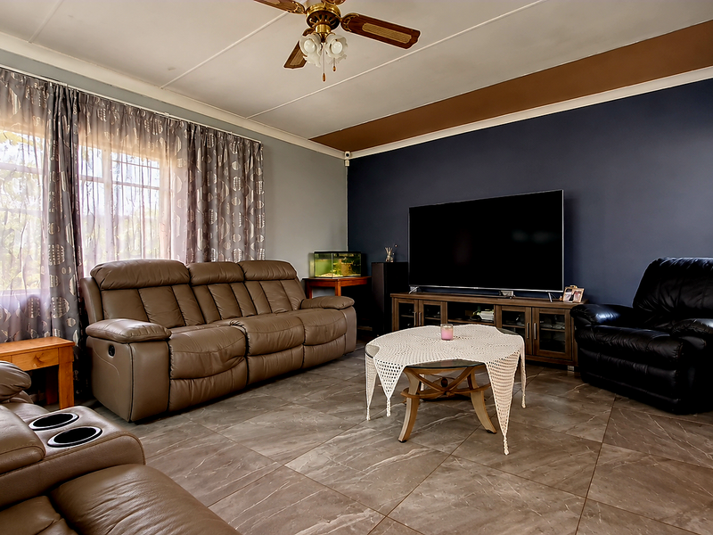 A spacious living room featuring tiled flooring, a ceiling fan, and a dark accent wall, providing a comfortable and functional family living space.