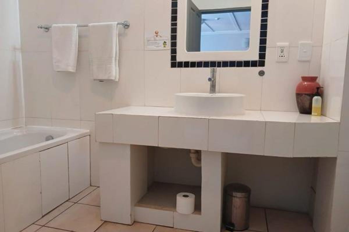 Bathroom featuring a tiled vanity with a vessel sink, a bathtub, and wall-mounted towel rail, presenting a functional but dated aesthetic.