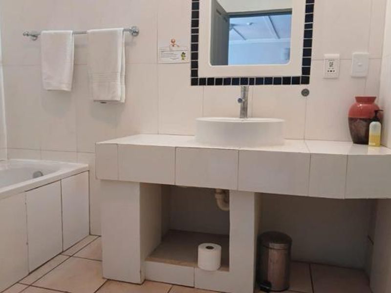 Bathroom featuring a tiled vanity with a vessel sink, a bathtub, and wall-mounted towel rail, presenting a functional but dated aesthetic.