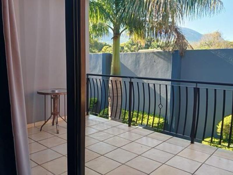 A private balcony featuring tiled flooring and a secure metal balustrade, offering an outdoor space with views of the surrounding garden and boundary wall.