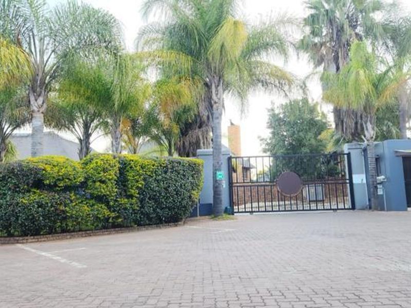 Front entrance view of the apartment complex featuring a paved driveway, secure gated access, and established garden landscaping.