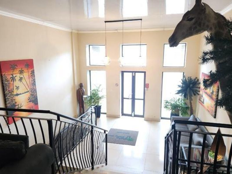 Spacious apartment building entrance foyer featuring a wrought iron staircase, tiled flooring, and large windows providing ample natural light.