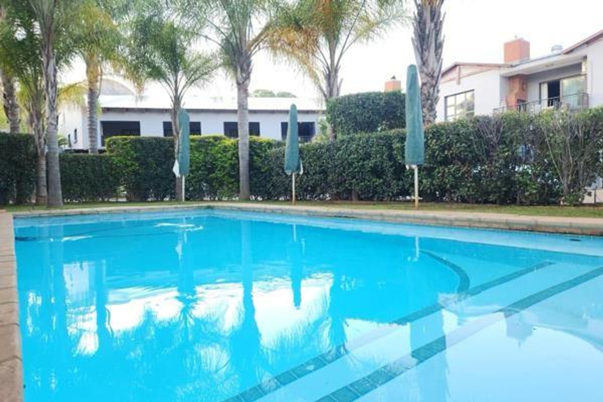 A well-maintained communal swimming pool area surrounded by established hedges and palm trees, providing a pleasant outdoor recreational space.