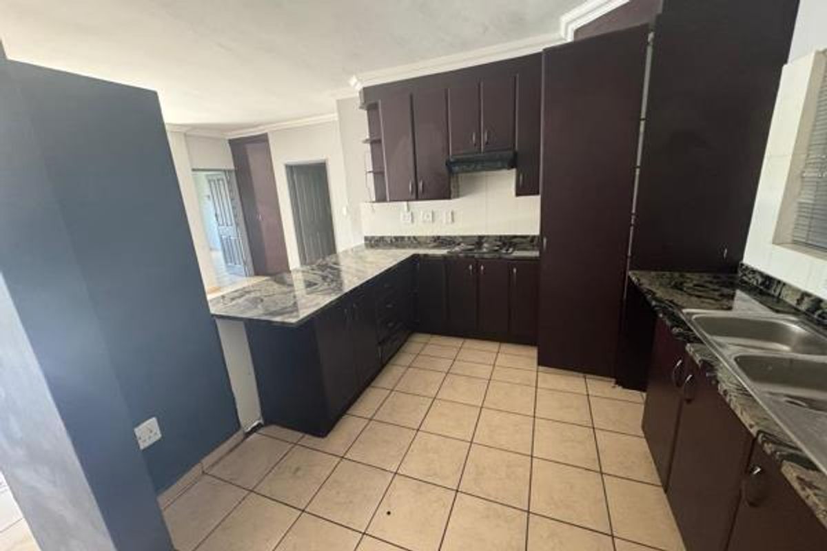 A functional kitchen featuring dark wood cabinetry, granite countertops, a double basin sink, and tiled flooring, offering a clean and practical workspace.