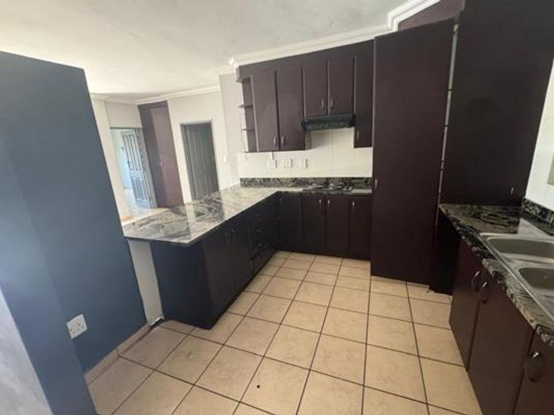 A functional kitchen featuring dark wood cabinetry, granite countertops, a double basin sink, and tiled flooring, offering a clean and practical workspace.