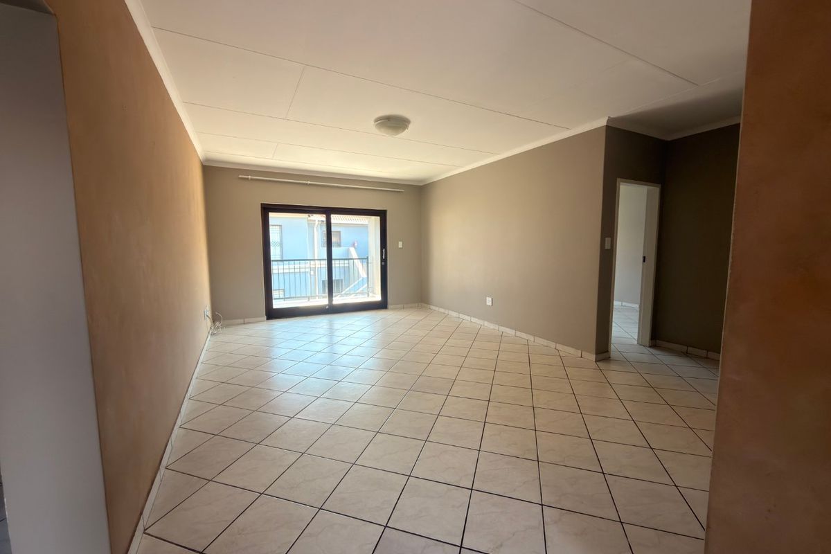 A spacious, empty living area featuring neutral-toned walls, tiled flooring, and a sliding glass door providing access to an outdoor balcony.